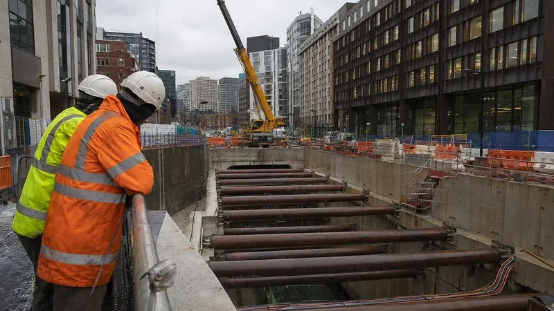 Innenstädtische Bahnbaustelle mit Schacht, Kran und Arbeitern in Warnkleidung